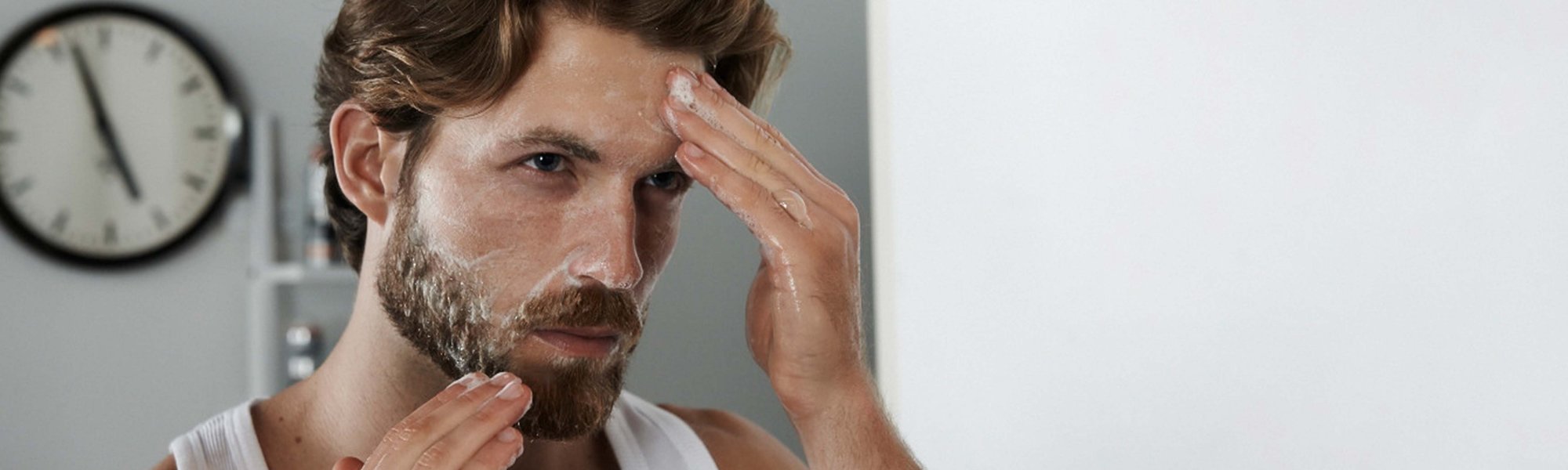 Ein Mann cremt sein Gesicht ein vor dem Spiegel stehend