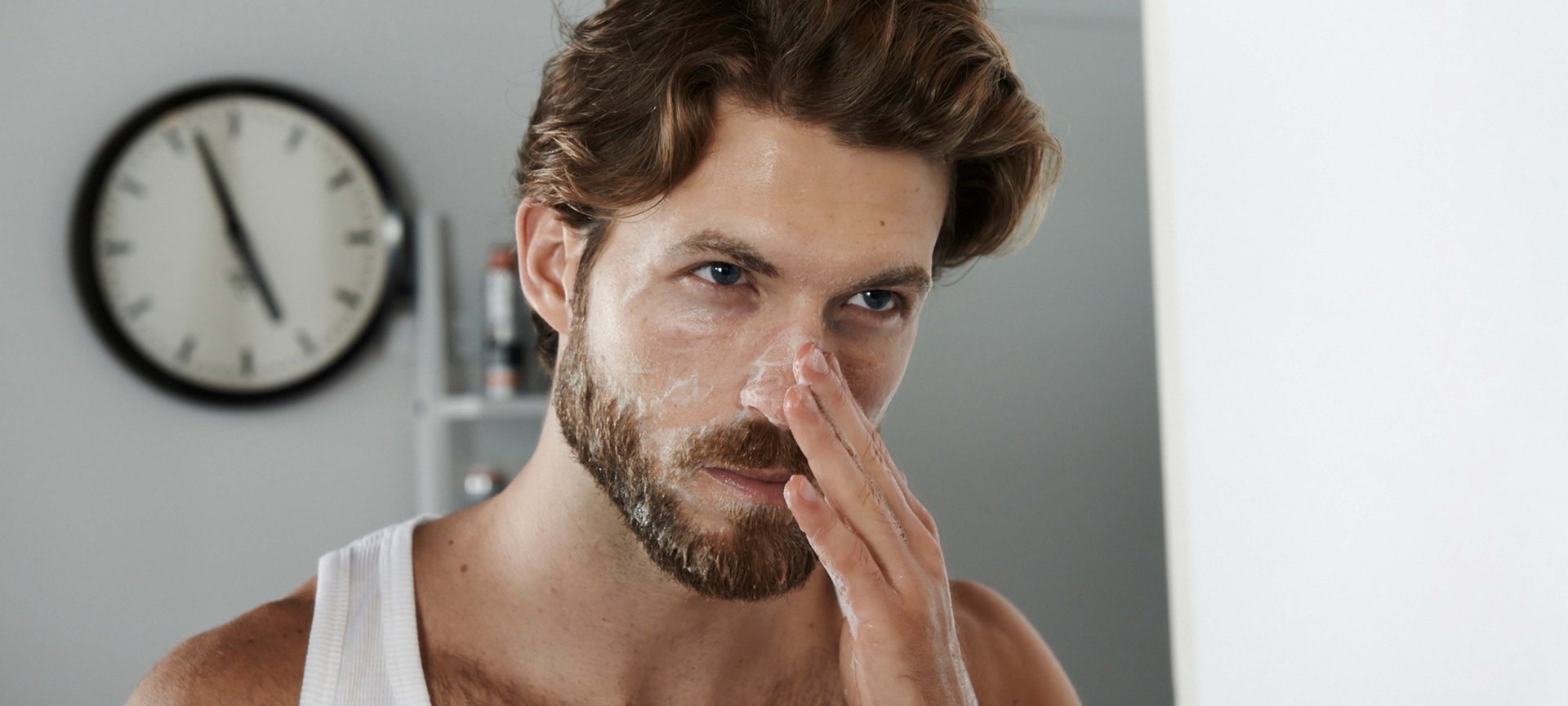 Ein Mann steht vor dem Spiegel und cremt sich seinen Nasenbereich ein