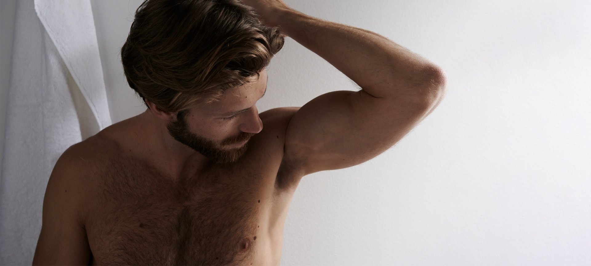 Ein Mann mit Vollbart riecht an seiner linken Achsel