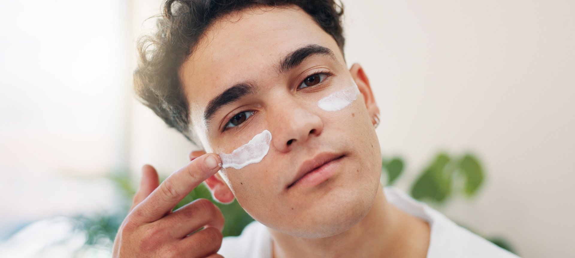 Ein junger Mann trägt mit einem Finger Sonnencreme auf seine Wangen auf