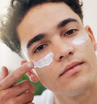 Ein junger Mann trägt mit einem Finger Sonnencreme auf seine Wangen auf
