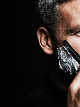 Mann vor schwarzem Hintergrund rasiert sich mit einem Rasiermesser