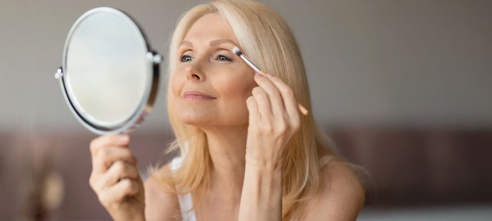Frau um die fünfzig, schminkt sich mit einem Handspiegel