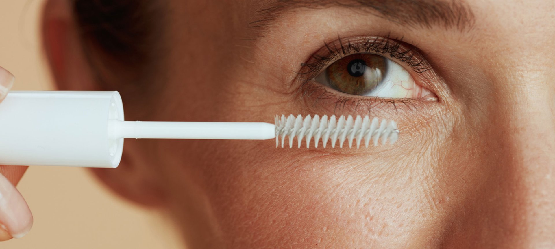 Nahaufnahme eines Frauenauges, dessen Wimpern mit einem durchsichtigen Mascara geschminkt werden.