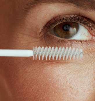 Nahaufnahme eines Frauenauges, dessen Wimpern mit einem durchsichtigen Mascara geschminkt werden.