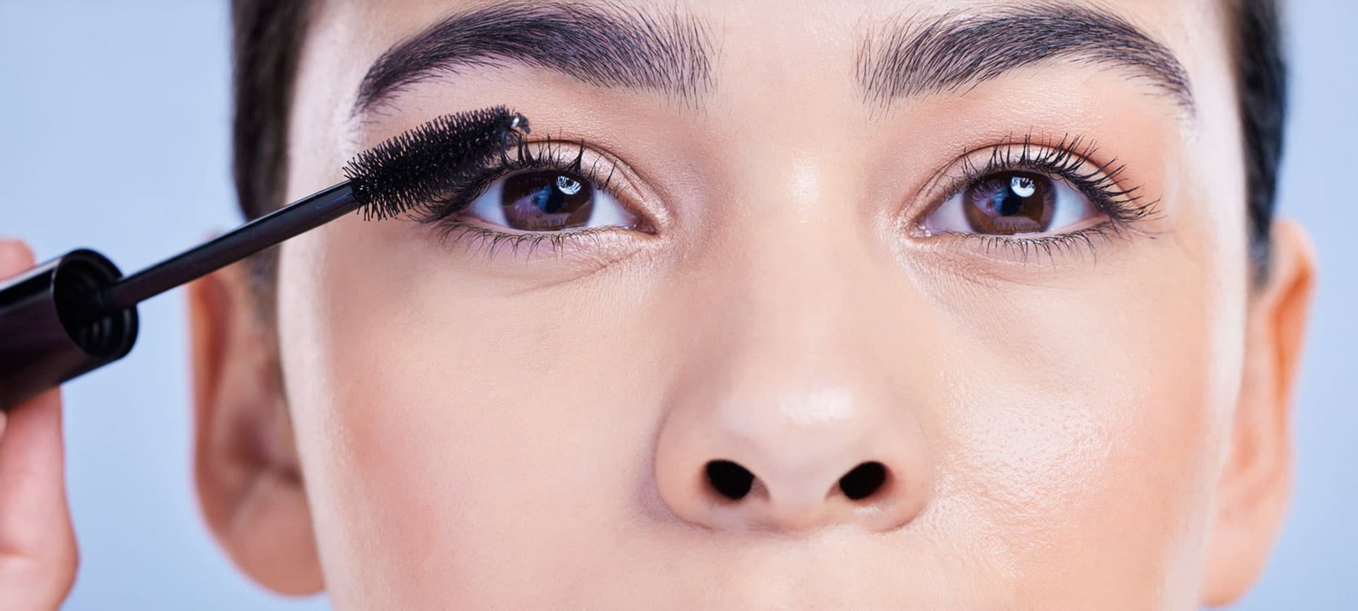 Closeup einer Frau mit braunen Augen, die sich mit Mascara die Wimpern schminkt.