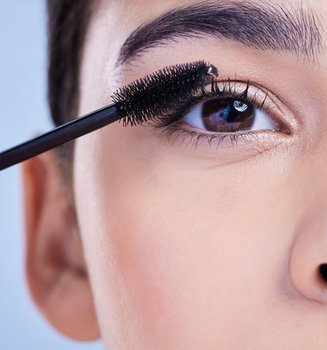 Closeup einer Frau mit braunen Augen, die sich mit Mascara die Wimpern schminkt.