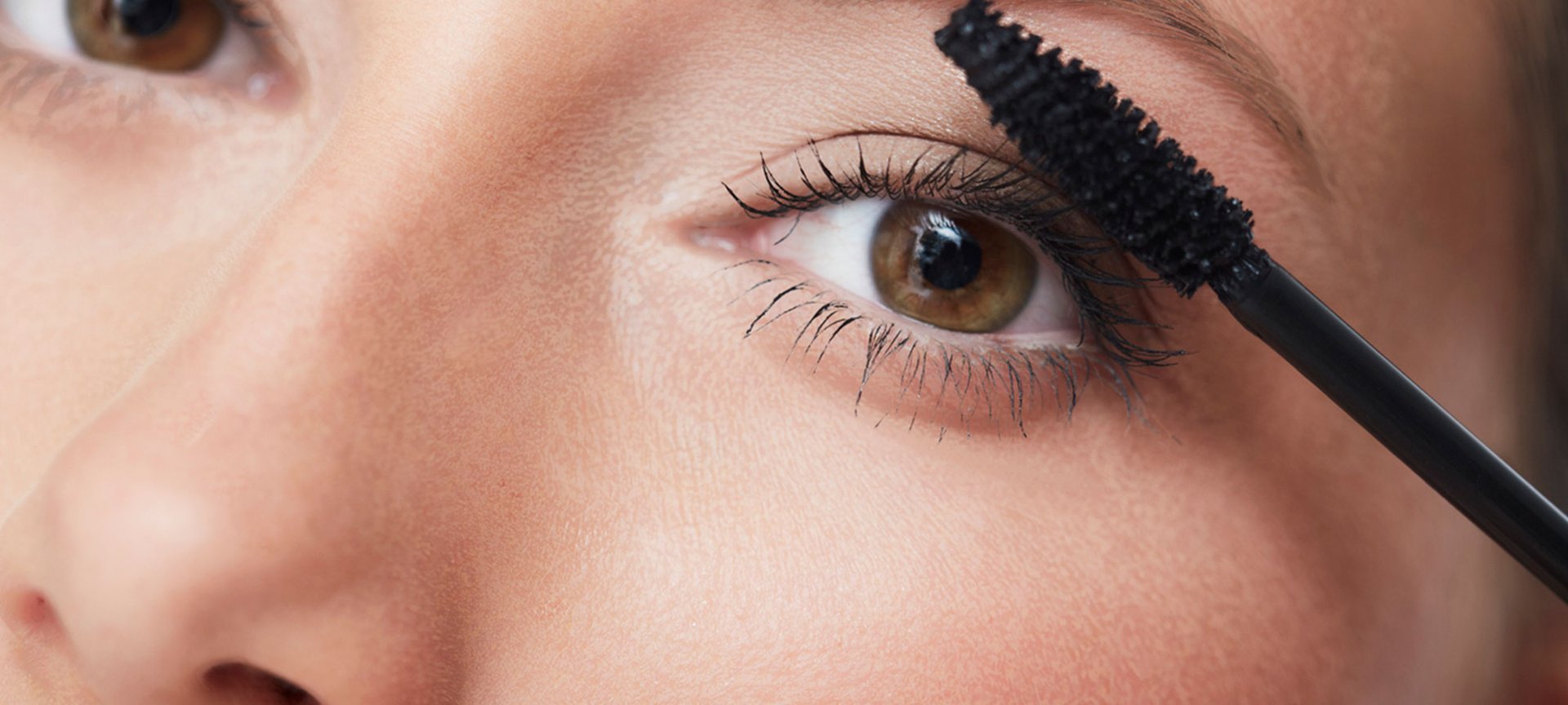 Eine junge Frau trägt einen Mascara auf ihre Wimpern auf