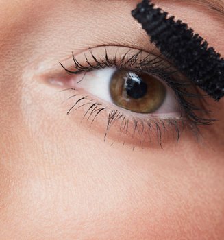 Eine junge Frau trägt einen Mascara auf ihre Wimpern auf