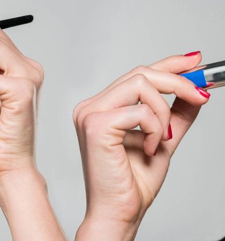 Zwei Gesichtshälften einer jungen Frau, die sich links Lidschatten und rechts blaue Mascara aufträgt