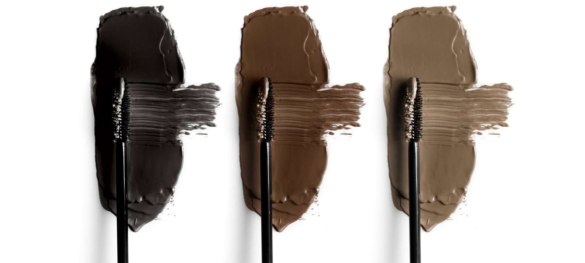 Drei Mascara-Bürsten liegen nebeneinander und wischen in den Farbklecksen Schwarz, Braun und Taupe jeweils von links nach rechts.