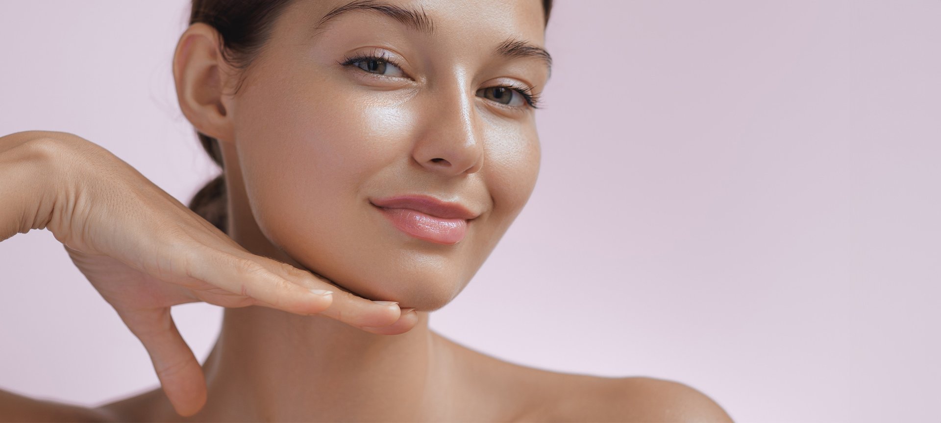 Junge Frau präsentiert ihr Glow-Make-up mit der rechten Hand unter dem Kinn.