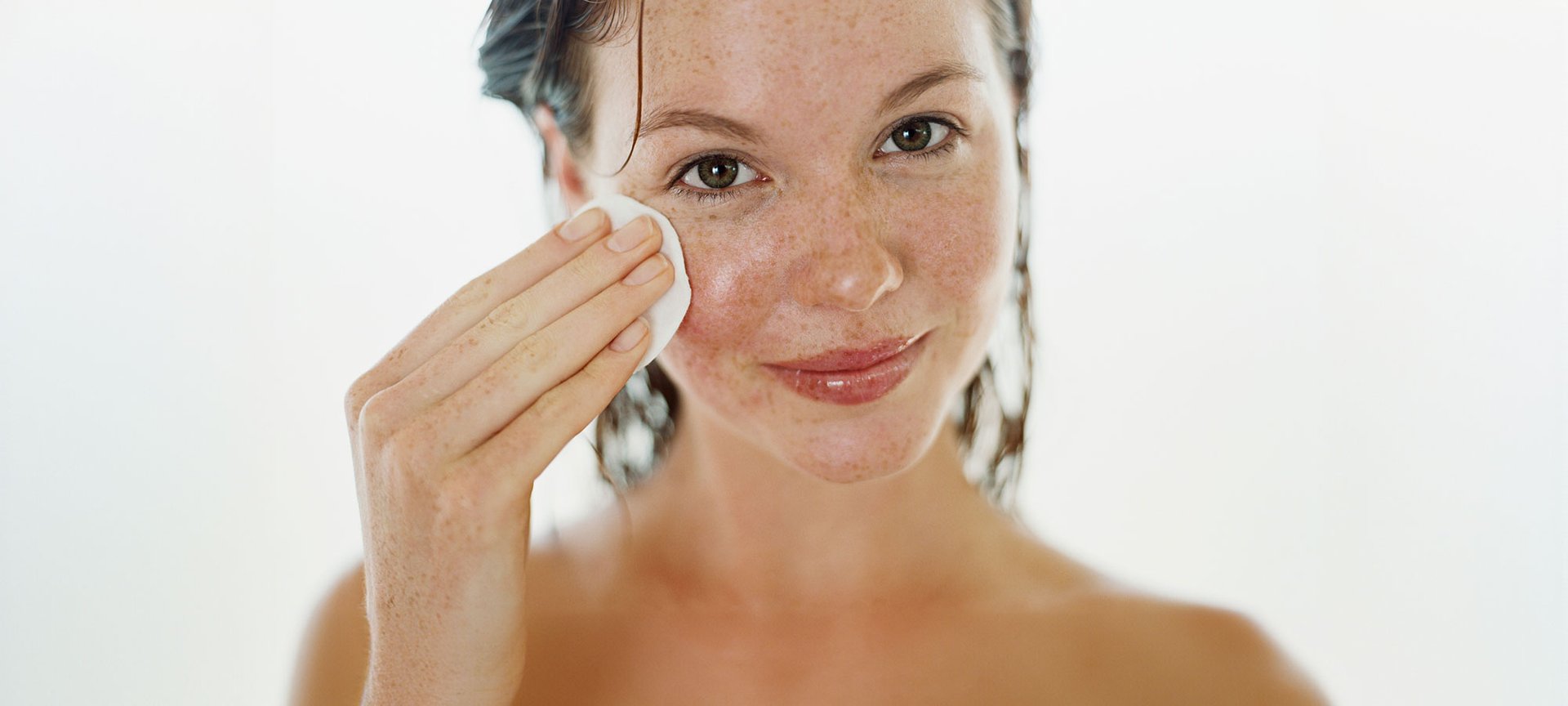 Junge Frau lächelt und reinigt ihr Gesicht mit einem Wattepad.