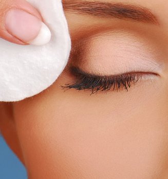 Closeup von den geschlossenen Augen einer Frau, die sich mit einem Wattepad Make-up an den Augen entfernt