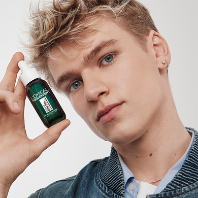 Ein junger Mann mit blonden Haaren hält das Anti-Unreinheiten Serum in seiner Hand