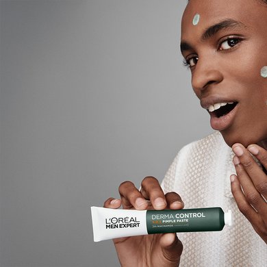 Junger Mann hat einige Spots mit S.O.S. 2in1 Anti-Pickel Paste auf de rWange und hält das Produkt in seiner Hand