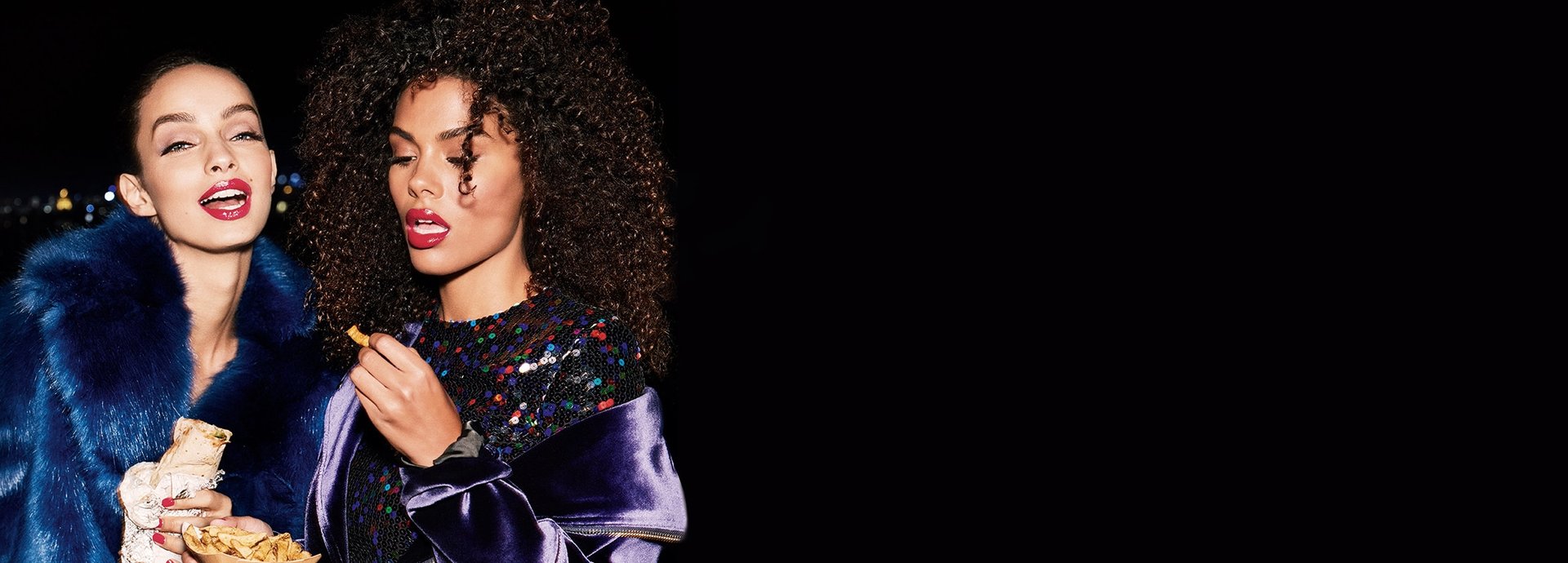 Zwei geschminkte und gestylte Frauen essen nachts einen Wrap und Pommes Frites. 