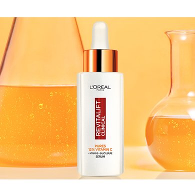Das Revitalift Clinical Vitamin C Serum steht neben Laborflaschen mit gelber Flüssigkeit
