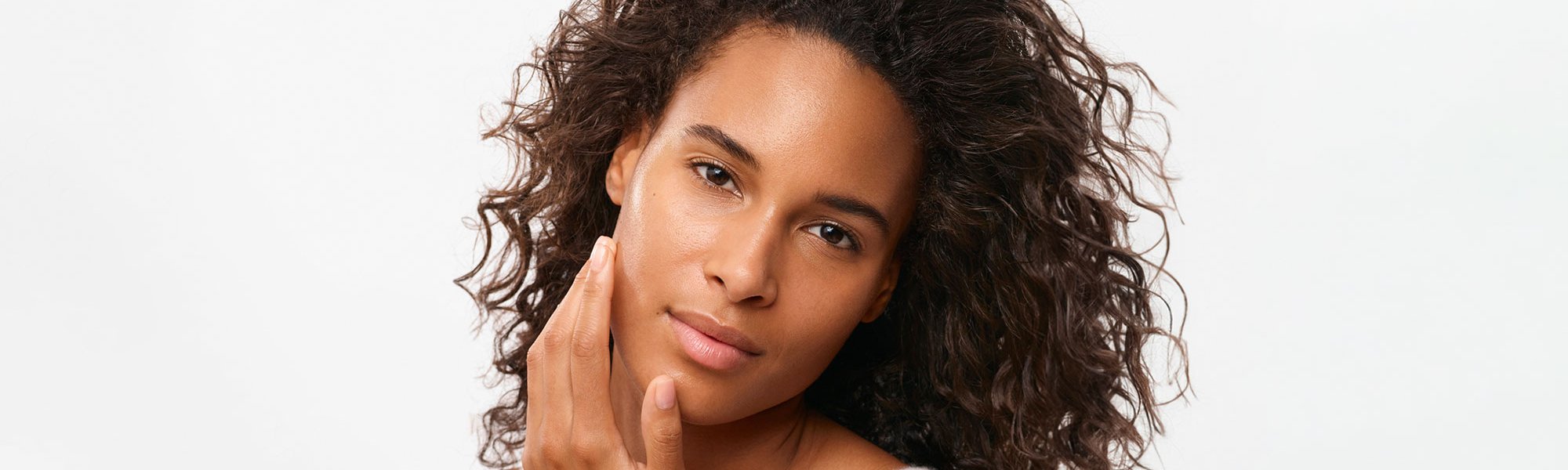 Eine junge Frau mit lockigen Haaren fährt sich über ihre linke Wange