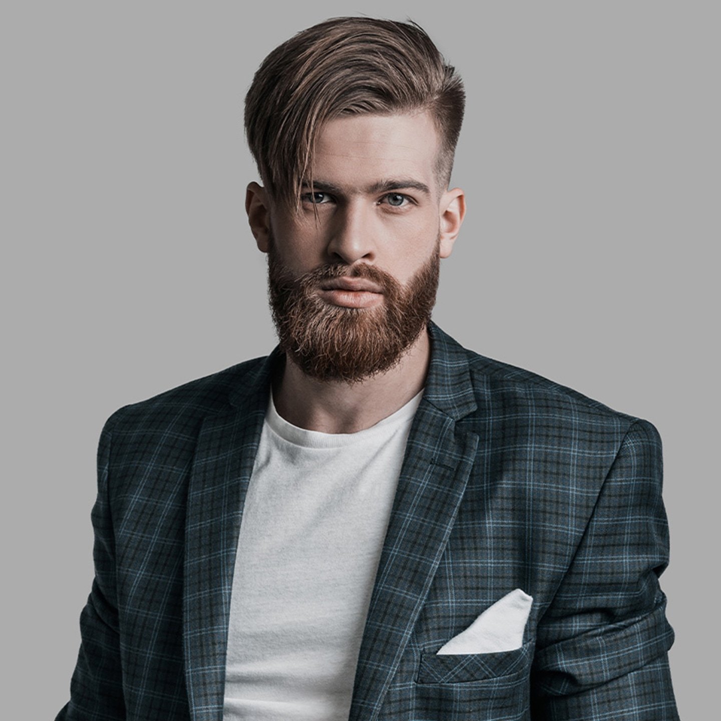 Junger Mann in kariertem Sakko mit gepflegtem Vollbart und gestylten Haaren
