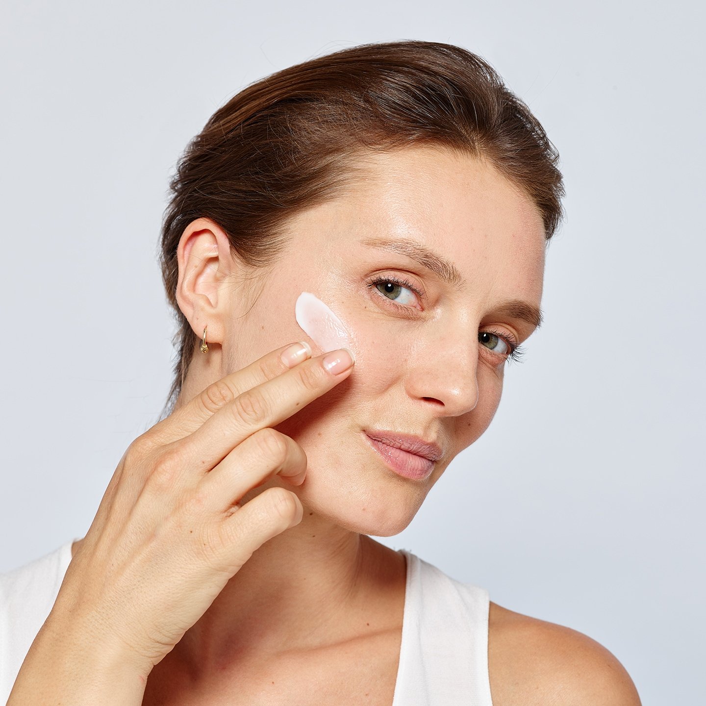 Eine junge Frau cremt ihre rechte Wangen ein