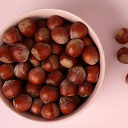 Fünf Haselnüsse neben einer Schale voller weiterer Haselnüsse
