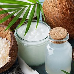 Kokosnüsse und Kokospalmenblatt neben Gefäßen mit Kokosöl