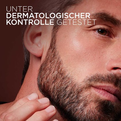 Nahaufnahme eines Mannes, der mit der Hand an seinen gepflegten, dichten Bart fasst. Oben links steht der weiße Text „UNTER DERMATOLOGISCHER KONTROLLE GETESTET“