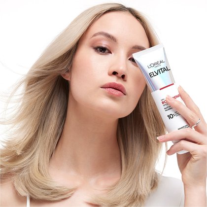Model haelt Elvital Bond Repair Spuelung Verpackung vor ihr Gesicht