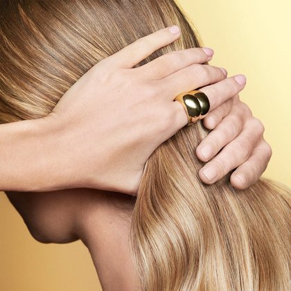 Junge Frau fasst ihre langen blonden Haaren zusammen