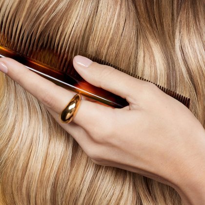 Eine Hand führt einen Kamm durch lange goldblonde Haare