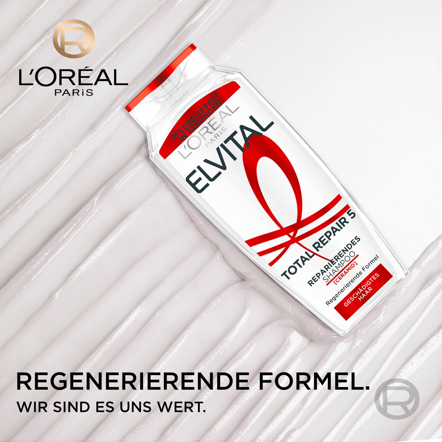 Schräg liegende Flasche des Elvital Total Repair 5 Reparierenden Shampoos auf einer weißen, cremigen Pflege-Textur mit dem L'Oréal Paris Logo und dem Slogan „Regenerierende Formel. Wir sind es uns wert.“.