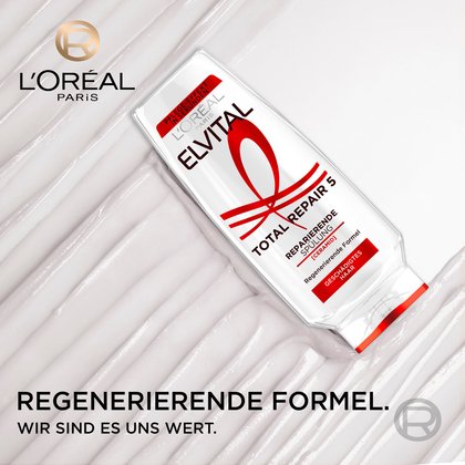 Schräg liegende Flasche der Elvital Total Repair 5 Reparierenden Spülung auf einer weißen, cremigen Textur mit dem Slogan „Regenerierende Formel. Wir sind es uns wert.“.