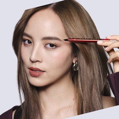 Eine Frau mit blonden Haaren hält den L'Oréal Paris Augenbrauenstift in der Nuance Blonde neben ihr Gesicht.