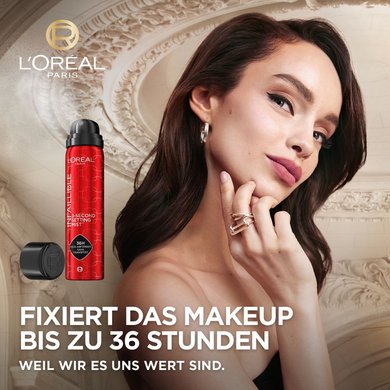 Model posiert vor einem Hintergrund mit Pariser Stuckverzierungen. Daneben ein Packshot eines Fixiersprays 'FIXIERT DAS MAKEUP BIS ZU 36 STUNDEN: weil wir es uns wert sind.'
