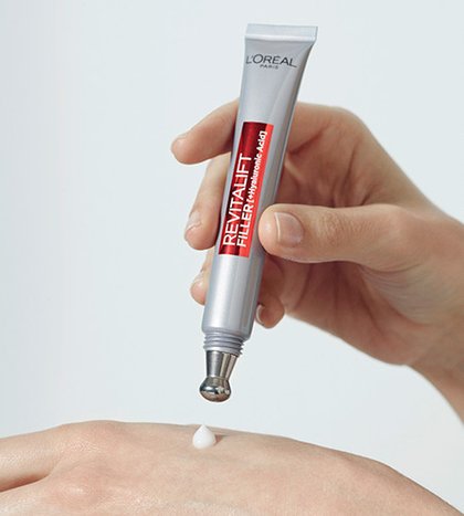 Eine Hand drueckt einen Tropfen Revitalift Filler HA aufpolsternde Pflege fuer das Auge auf den anderen Handruecken