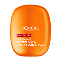 Eine Frau hält das orangefarbene L'Oréal Revitalift Daily Fluid vor ihr Auge und lächelt.