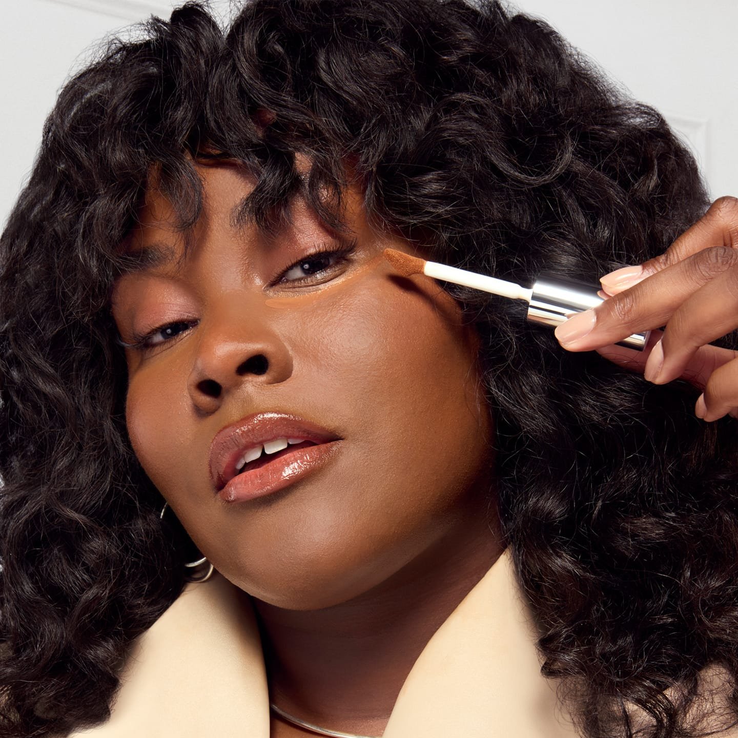 Eine junge Frau trägt mit einem Concealerpinsel Radiant Serum Concealer 10D Deep auf ihre Wange auf