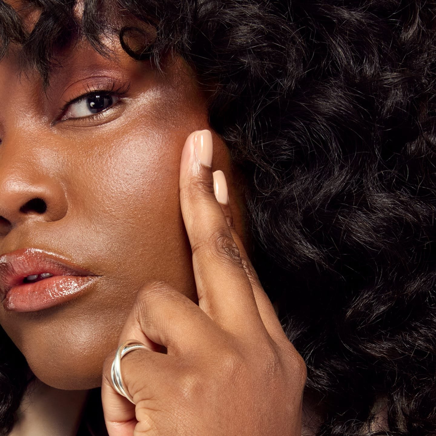 Eine junge Frau betrachtet ihre linke Wange nach Auftragen des Radiant Serum Concealer 11N Deep