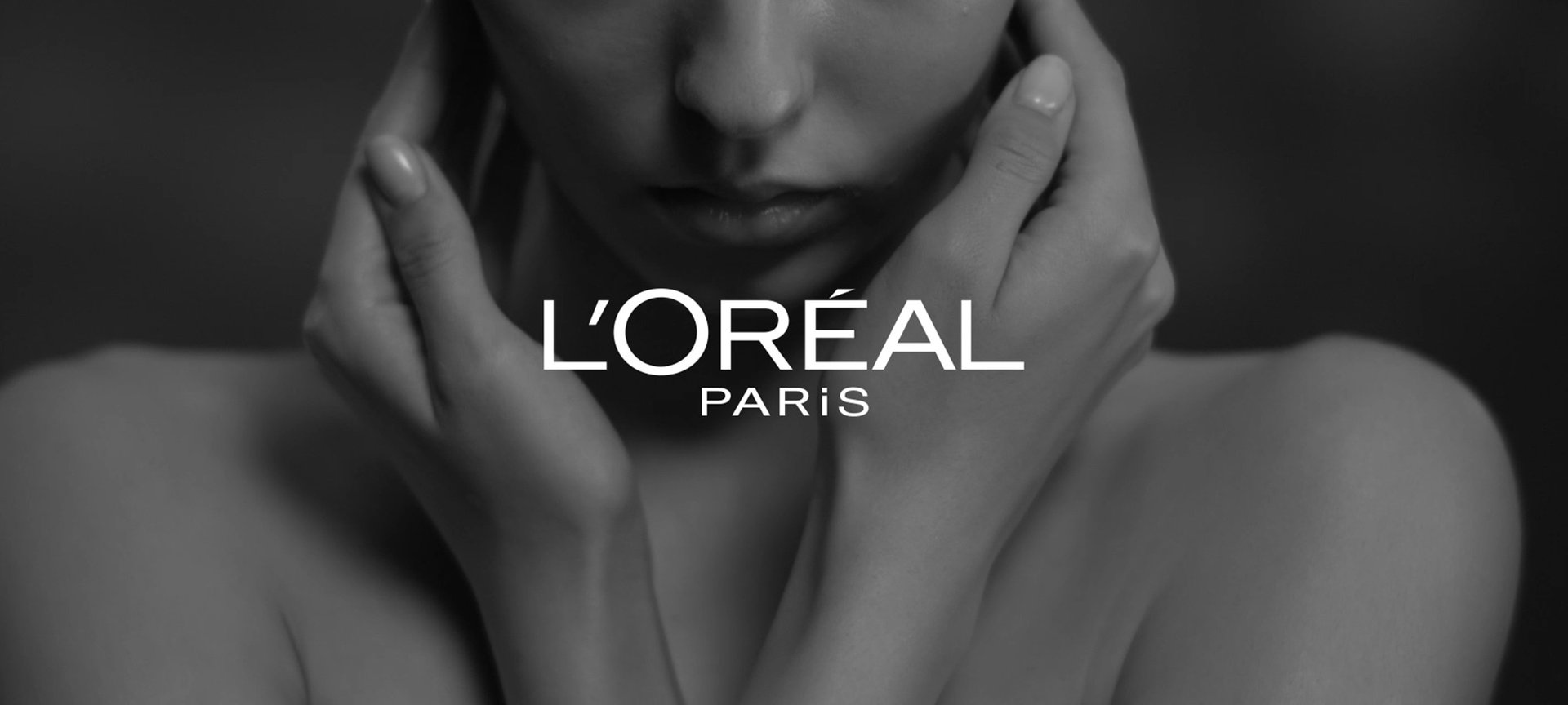 L'Oréal Paris Logo, im Hintergrund eine Frau, die ihre Hände an ihr Gesicht hält